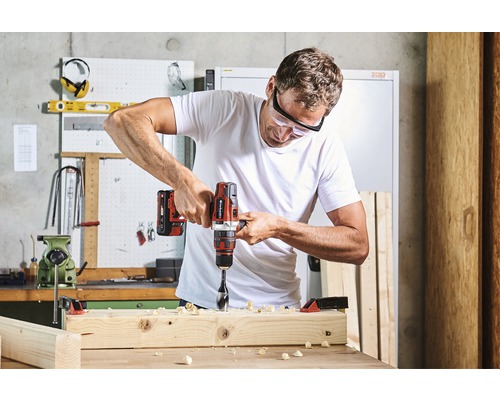 Muž vŕta vŕtačkou do drevenej dosky v dielni