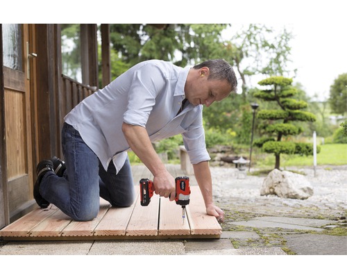 Muž montuje drevené dlaždice pomocou akumulátorového skrutkovača vonku