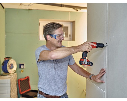Muž skrutkuje sadrokartónovú stenu pomocou akumulátorového skrutkovača