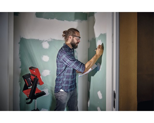 Muž s ochrannými okuliarmi, poznámkovým blokom a perom pred nedokončenou stenou a stavebným reflektorom