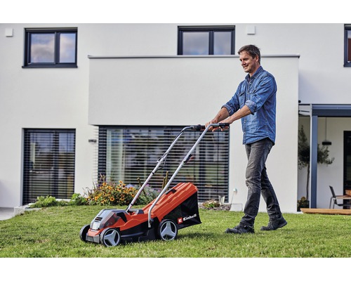 Muž používa kosačku na trávu Einhell v záhrade pred domom.