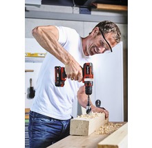 Muž vŕta akumulátorovým skrutkovačom otvor do kusu dreva.