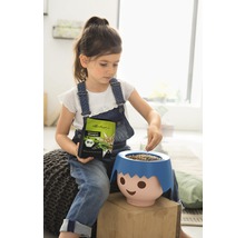 Dievča plní kvetináč v tvare tváre semenami trávy, drží obal so semenami, bio pečať