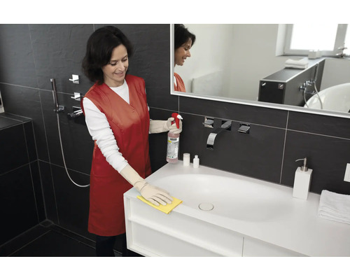 Žena čistí umývadlo čistiacim prostriedkom a handrou v kúpeľni.