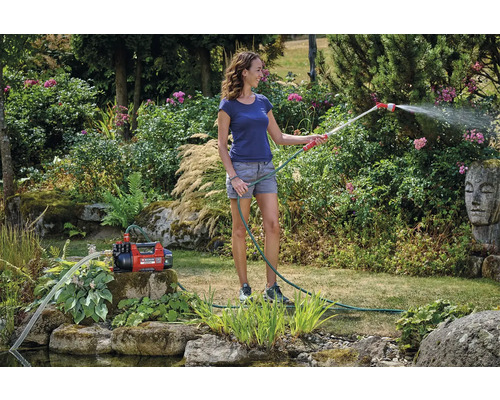 Žena zavlažuje záhradu záhradným čerpadlom a záhradnou hadicou