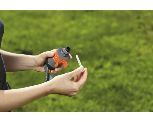 Ruky vkladajú hnojivovú tyčinku do zavlažovacieho zariadenia pre záhradu