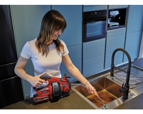 Žena používa inštalatérske pero Einhell na uvoľnenie odpadovej rúry.