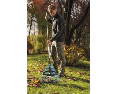 Muž hrabe lístie hrabľami na lístie v záhrade.