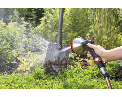 Osoba čistí špinavú lopatu pomocou postrekovača Gardena v záhrade.