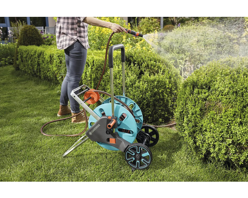 Žena zalieva záhradu pomocou vozíka na hadicu a hadice