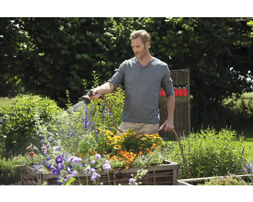 Muž zalieva kvety záhradnou hadicou v záhrade.