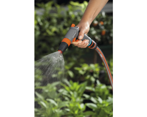 Ruka drží záhradný postrekovač, ktorý strieka vodu.