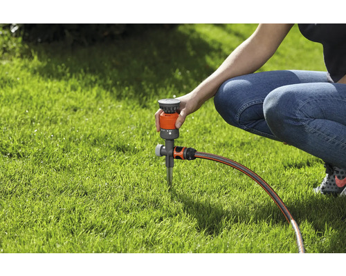 Osoba nastavuje zavlažovač trávnika na trávniku.