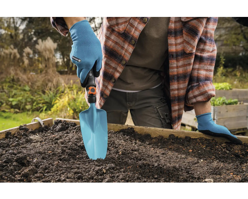 Osoba v záhradných rukaviciach používa záhradnú lopatku vo vyvýšenom záhone.