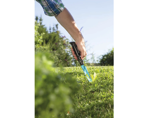 Záhradná scéna s rukou používajúcou vytrhávač buriny v trávniku