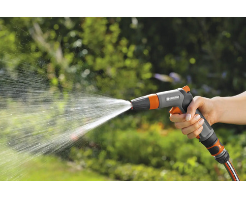 Ruka drží záhradnú striekaciu pištoľ, z ktorej strieka voda.