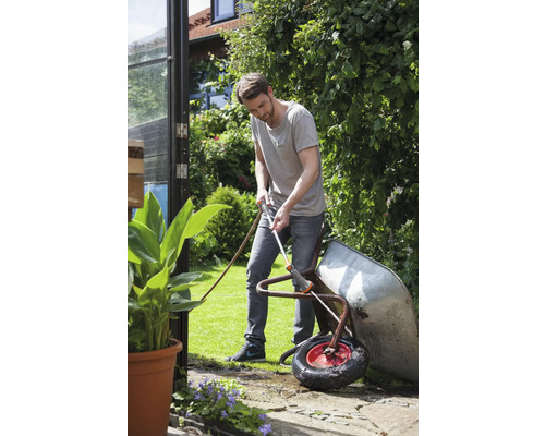 Muž čistí záhradnou hadicou koliesko na záhrade.