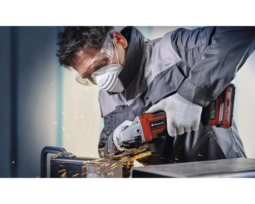 Muž brúsi kov pomocou akumulátorovej uhlovej brúsky Einhell a nosí ochranné pomôcky.