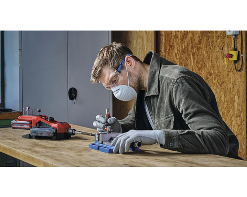 Muž pracuje s akumulátorovým multifunkčným nástrojom, chránený bezpečnostným vybavením.