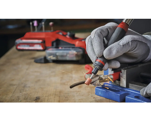 Osoba brúsi kov multifunkčným nástrojom a ochrannými rukavicami v dielni.