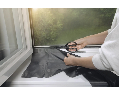 Osoba strihá nožnicami zatemňovaciu roletu na okne.