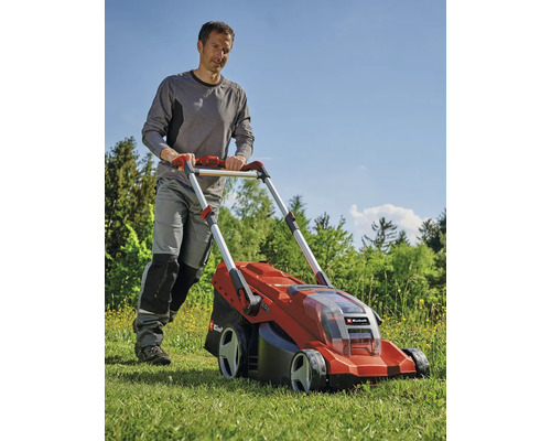 Muž tlačí červenú akumulátorovú kosačku na trávu v záhrade