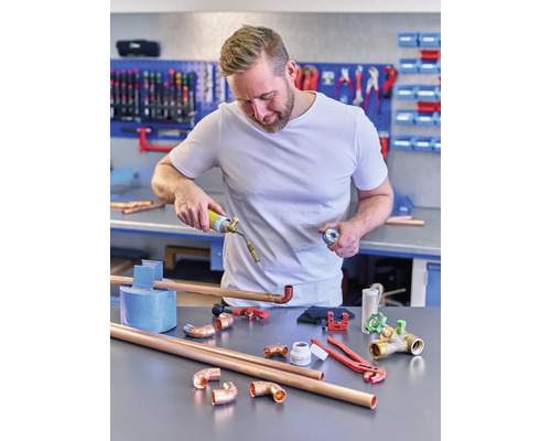 Muž spájkuje medené rúrky s plynovým horákom v dielni.