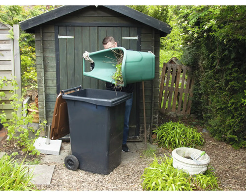 Muž vysýpa zelený odpad do smetnej nádoby v záhrade