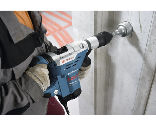 Muž vŕta diery do betónovej steny pomocou vŕtacieho kladiva Bosch.