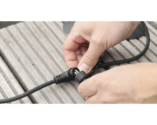 Muž pripája čierny kábel ku konektoru na drevenom povrchu.