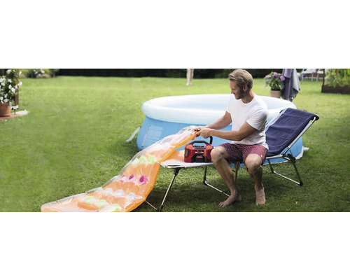 Muž nafukuje vzduchový matrac vzduchovou pumpou v záhrade, v pozadí bazén