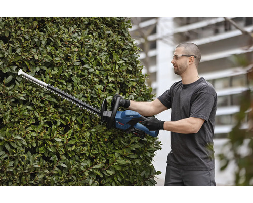 Muž strihá živý plot pomocou akumulátorových nožníc na živý plot