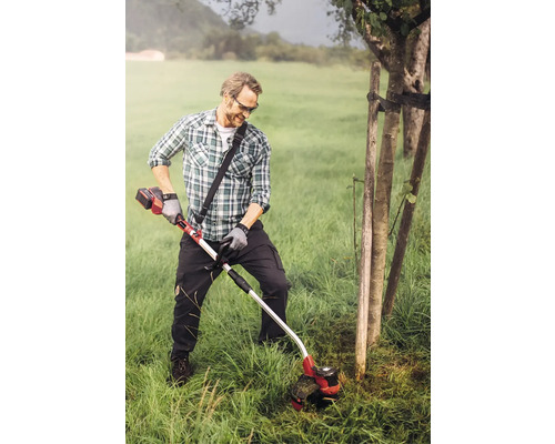 Muž strihá trávu akumulátorovým vyžínačom v záhrade.