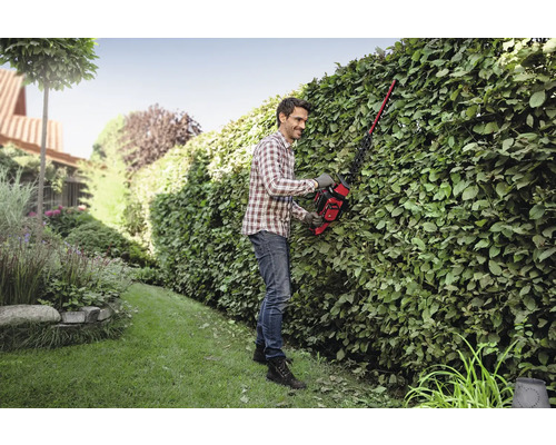 Muž strihá živý plot v záhrade pomocou nožníc na živý plot.