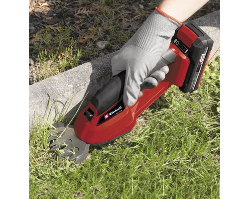 Osoba používa akumulátorové nožnice na trávu Einhell na strihanie trávy pozdĺž okraja trávnika.