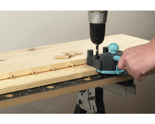 Osoba používa kolíkovací prípravok s vŕtačkou na drevenej doske.