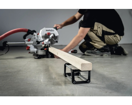 Osoba obsluhuje pokosovú pílu Metabo na rezanie kusa dreva, ktorý leží na podperu obrobku.