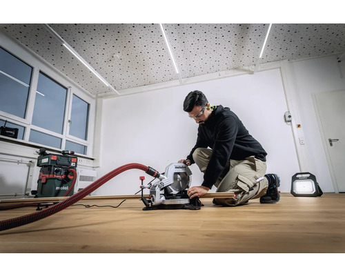 Muž pracuje s pokosovou pílou Metabo vo svetlej miestnosti. V pozadí je vidieť vysávač a stavebné svetlo.