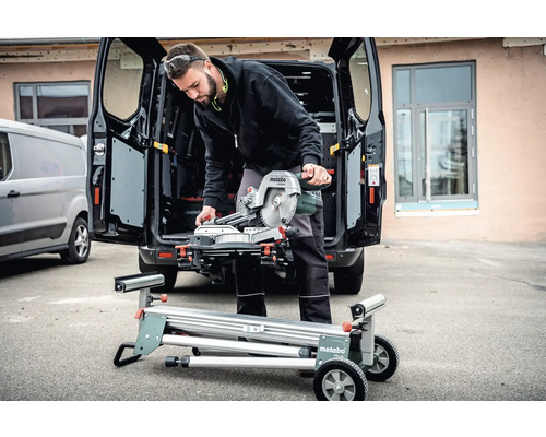 Muž s pokosovou pílous Metabo na pílovom stole pred dodávkou