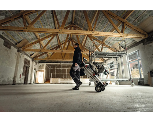 Muž prepravuje lešenie na kolieskach v miestnosti s drevenými trámami.