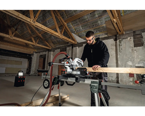 Muž pracuje s pokosovou pílou Metabo v hrubej stavbe na rezanie drevenej dosky.