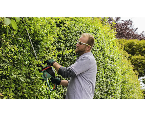 Muž strihá živý plot nožnicami na živý plot.