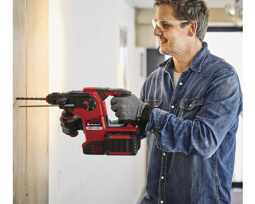 Muž vŕta dieru do steny pomocou akumulátorového vŕtacieho kladiva Einhell Herocco.