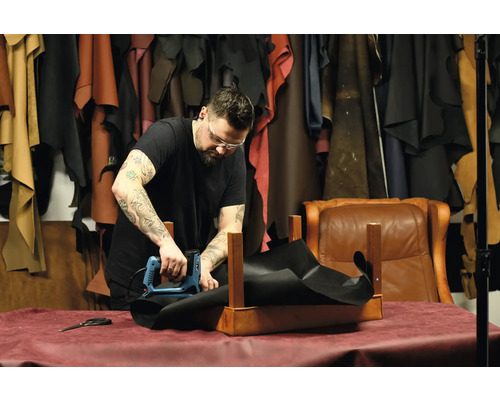 Remeselník pripevňuje elektrickou sponkovačkou čierny kus látky k drevenému rámu v dielni.