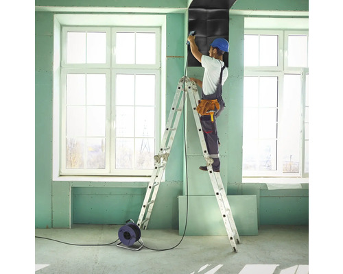 Remeselník pripevňuje izolačnú dosku na stavenisku pomocou rebríka.