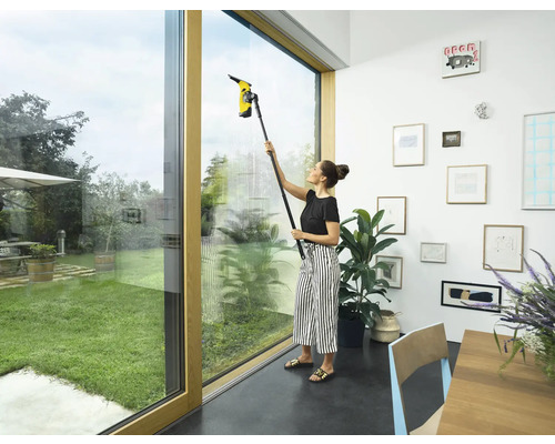 Žena čistí okná s okenným vysávačom v interiéri.