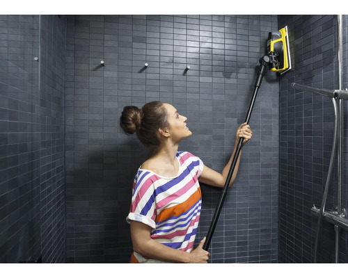 Žena čistí obkladačkovú sprchu stierkou na okná s teleskopickou tyčou