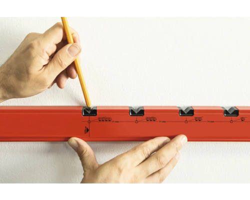 Ruka s ceruzkou označuje otvory pre hmoždinky na stene pomocou vŕtacej šablóny.