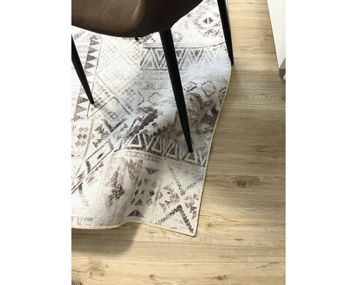 Dekoratívny koberec s geometrickými vzormi pod stoličkou na drevenej podlahe.