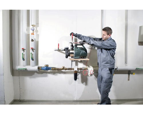 Inštalácia záhradného čerpadla remeselníkom na stenu s rúrkami.